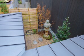 A rooftop garden with a stone lantern, bamboo fence, and a small tree.
