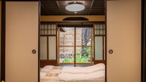 Een traditionele Japanse kamer met tatami vloeren, een laag bed met witte beddengoed en schuifdeuren met uitzicht op een tuin.