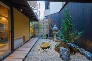 A narrow courtyard with a wooden deck, a stone basin, and a small tree.