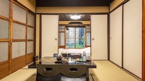 Een traditionele Japanse kamer met tatami vloerbedekking, een lage tafel met een waterfles, en uitzicht door een shoji scherm naar buiten.