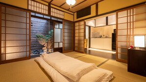 Um quarto japonês tradicional com tatames, uma cama baixa, portas deslizantes e uma pequena escrivaninha com uma lâmpada.