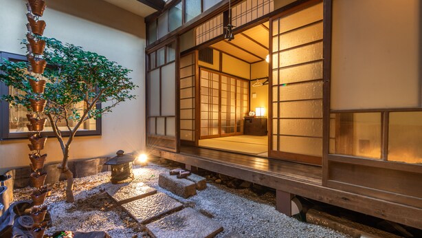 Um quarto tradicional japonês com piso de tatame, portas deslizantes shoji e um pequeno jardim com uma árvore e lanternas de pedra.