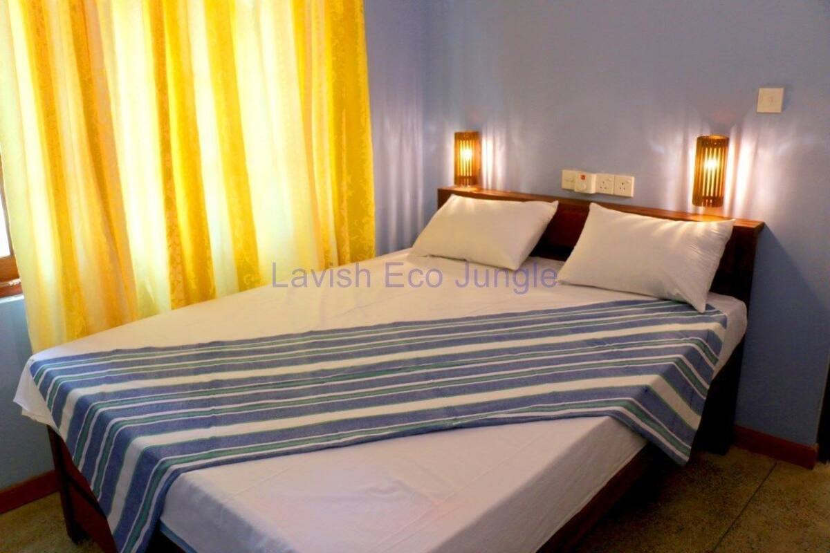 Una cama con colcha a rayas, dos lámparas de noche y una ventana con cortinas amarillas.