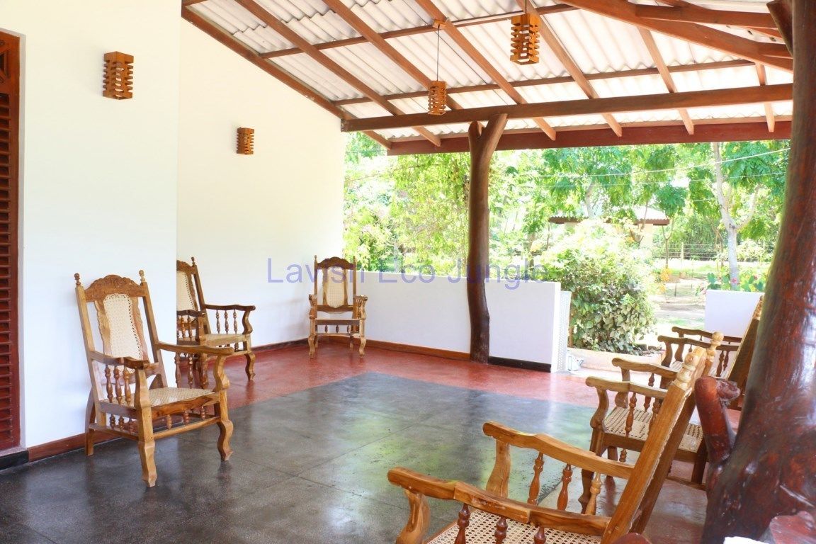 A covered patio area with wooden chairs and a view of greenery outside.