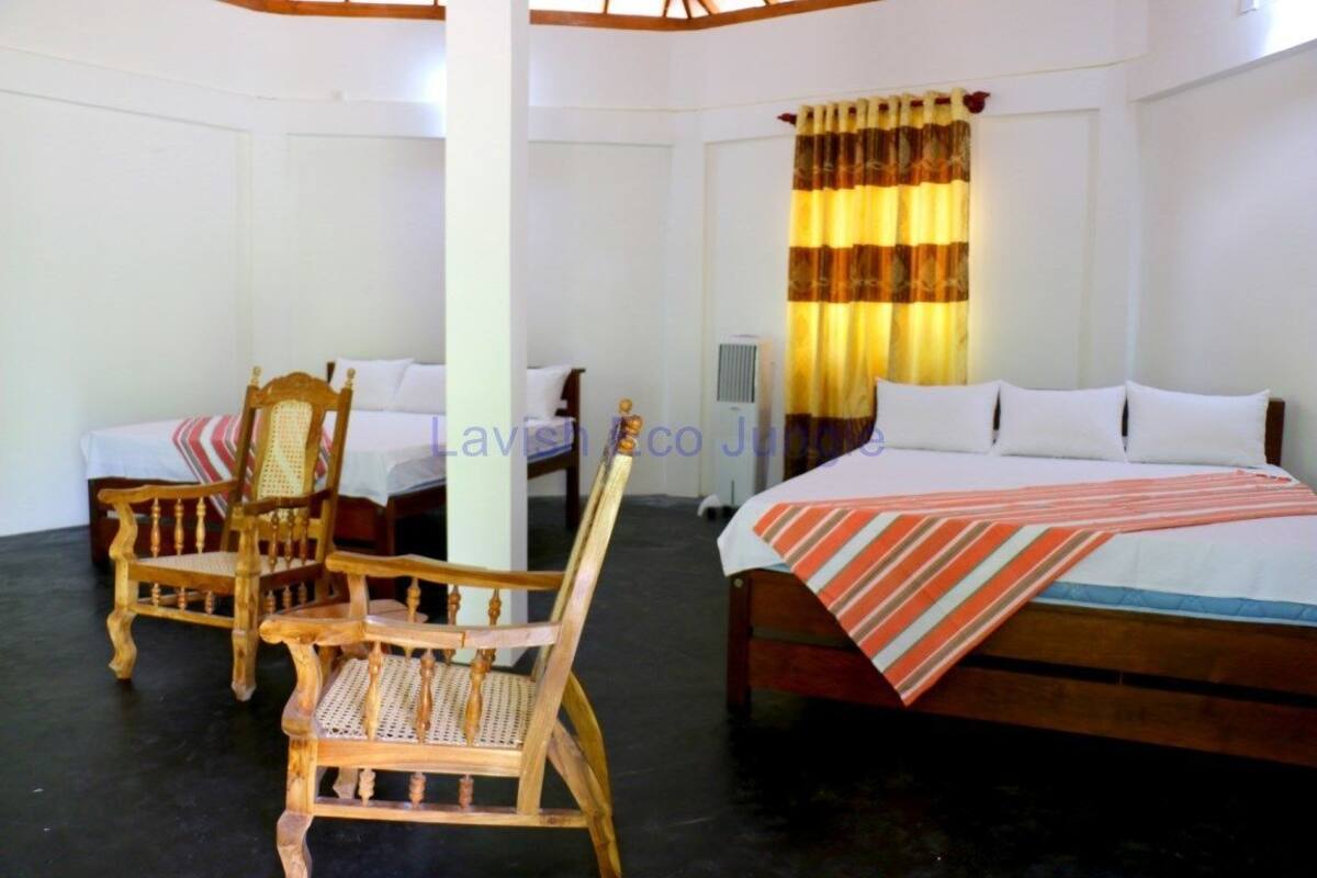 Habitación de hotel con cama, dos sillas de madera, una mesita y una ventana con cortinas.
