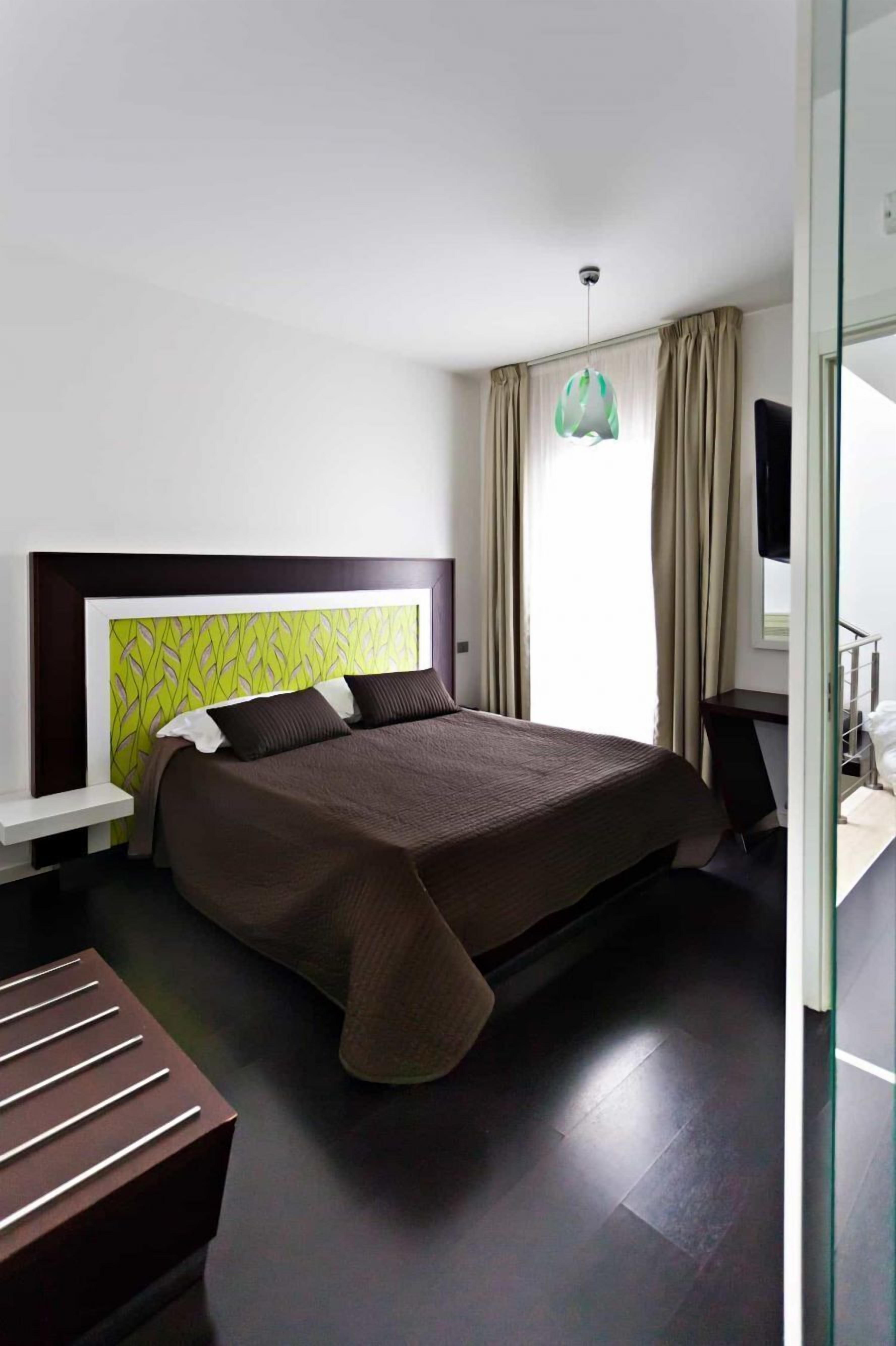 A modern hotel room with a large bed, a bedside table, a desk, and a window with curtains.