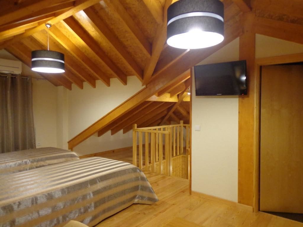 Un dormitorio con techo inclinado, vigas de madera, una cama con ropa de cama a rayas, un televisor montado en la pared y una puerta de madera.