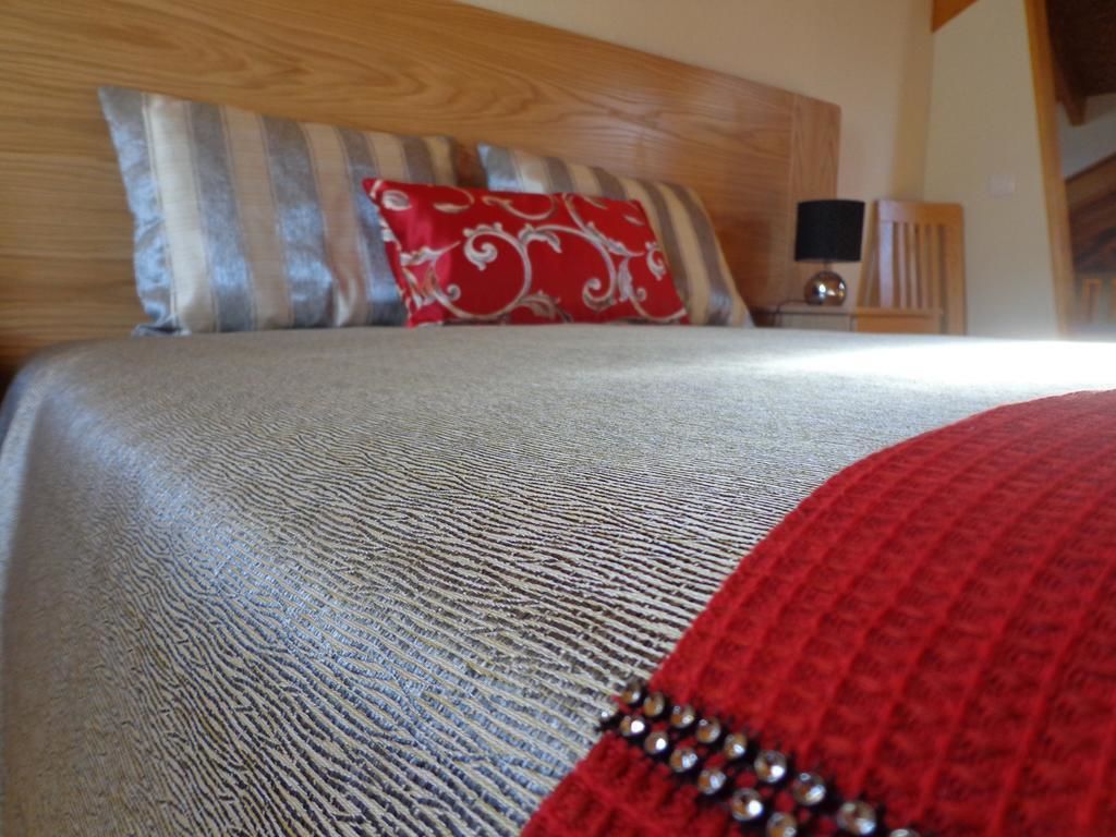 A bed with a textured grey duvet, a red pillow with a white pattern, and a wooden headboard.