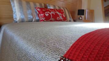 A bed with a textured grey duvet, a red pillow with a white pattern, and a wooden headboard.