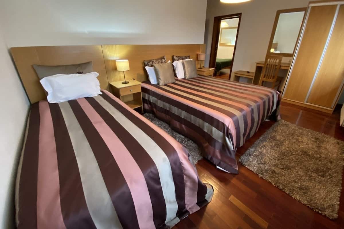 A hotel room with two beds, wooden headboards, a nightstand with a lamp, a mirror, and a wooden floor.