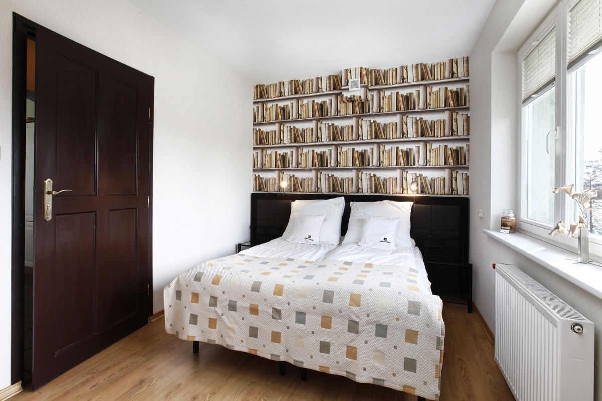 Une chambre avec une grande bibliothèque, un lit recouvert d’une couvre-lit à motifs et une fenêtre donnant sur un beau paysage.