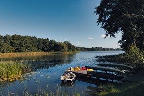 A calm lake with boats docked on a wooden pier, surrounded by lush greenery and a clear sky. - Port Rybaki (Brodnica)