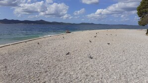 A pebbled beach with a clear sky and distant mountains.