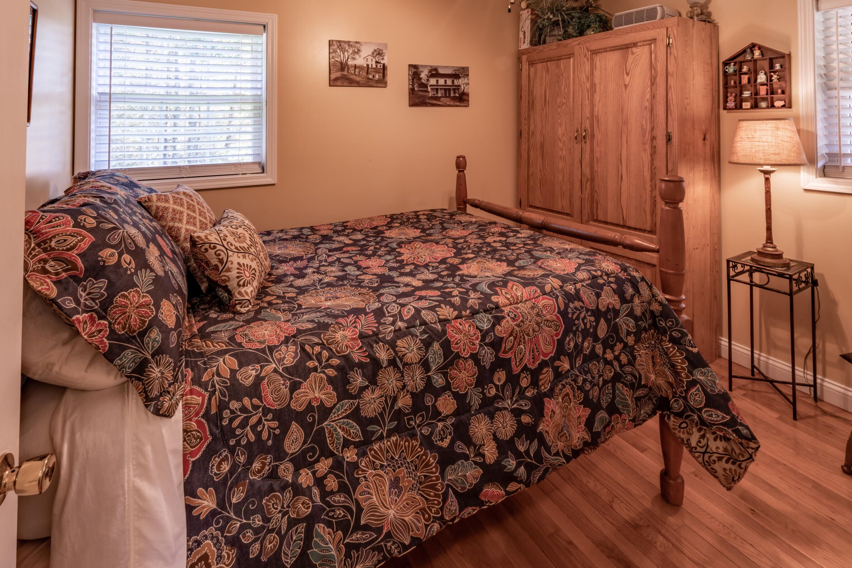 Une chambre à coucher avec une couvre-lit à motifs floraux, une armoire en bois et une petite table avec une lampe.