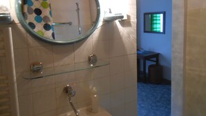 Un bany amb un mirall rodó, una dutxa i una prestatgeria de vidre.