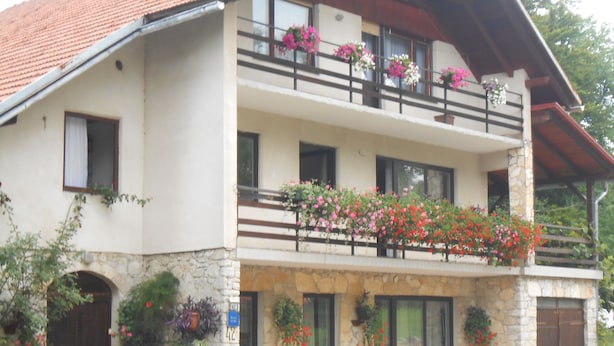 Un edifici de dues plantes amb façana de pedra, diversos balcons amb jardineres i una petita zona d'seients a l'exterior.