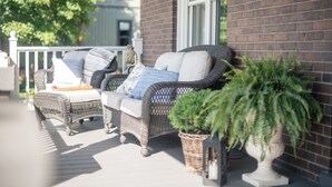 A wicker sofa with cushions, a potted plant, and a brick wall.