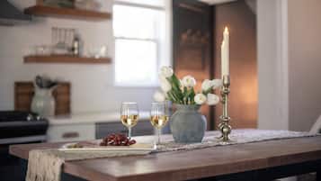 Une table à manger avec deux verres de vin blanc, un vase de fleurs blanches et une bougie allumée.