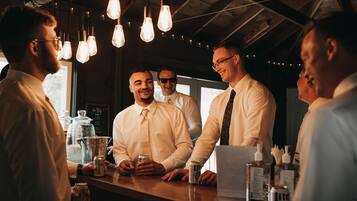 Un groupe d’hommes se tient debout au comptoir d’un bar, sous des luminaires suspendus et devant un plafond en bois.