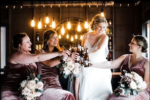 A group of people toasting with beer bottles in a warmly lit room with hanging light bulbs.
