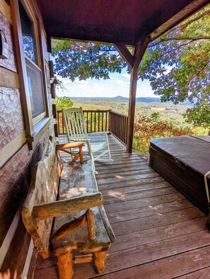 Una terraza de madera con un banco y una mesa, con vista a un paisaje pintoresco.