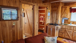 Interior de cabana de madeira, com sofá vermelho, área de cozinha e porta de madeira.