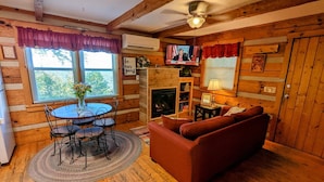 Interior acolhedor de uma cabana com mesa de jantar, cadeiras, sofá, lareira e televisão.
