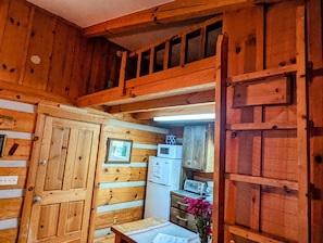 Innenansicht einer Holzhütte mit Küchenbereich, inklusive Kühlschrank, Mikrowelle und Holzschränken.