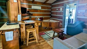 Un interior de cabaña con detalles de madera, una zona de cocina con pileta y estufa, una mesa de comedor con sillas y un sofá.