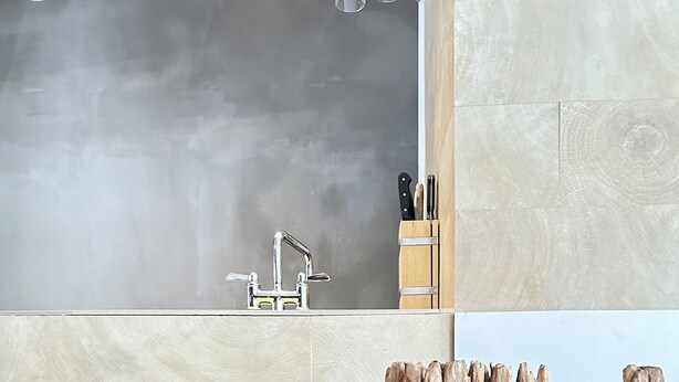 A modern kitchen with a large island, a sink, and wooden stools.