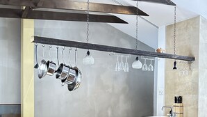 A modern kitchen with a built-in island, stainless steel pots, hanging wine glasses, and a wooden dining table.