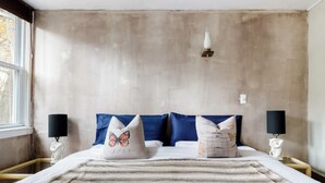 A bedroom with a large bed, two nightstands, a window, and a plain wall.