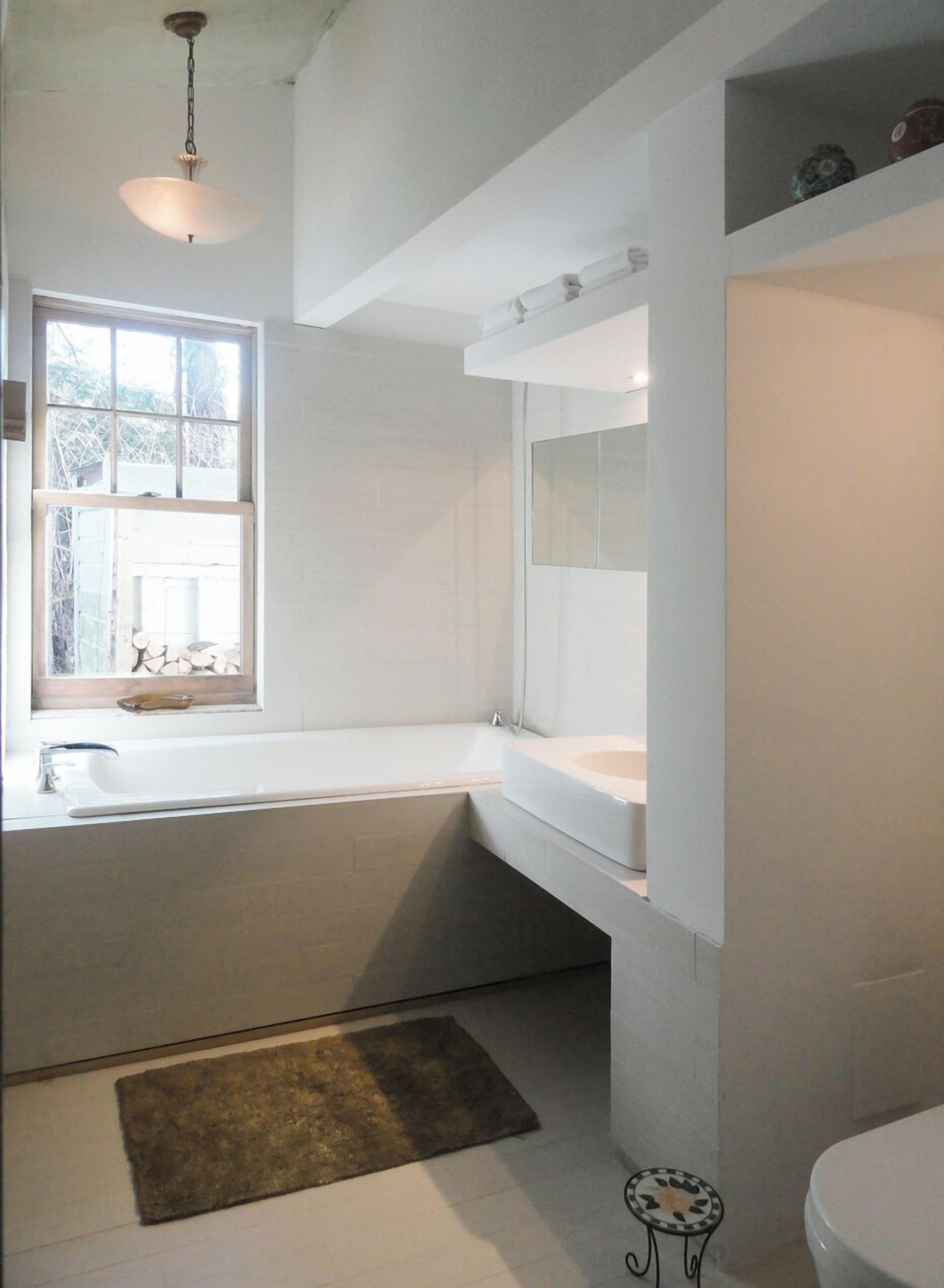 A modern bathroom with a bathtub, a toilet, and a window.