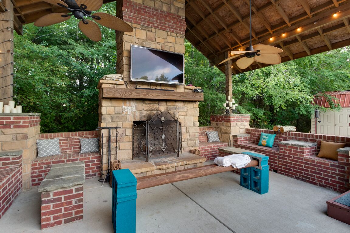 An outdoor patio with a stone fireplace, seating areas, and a television mounted above the fireplace.