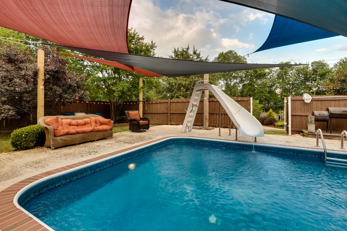 Un jardin avec une piscine, un toboggan, un coin salon confortable et un barbecue.