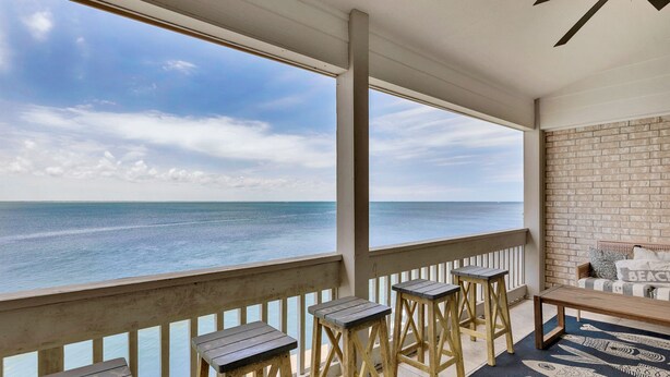 Ein Balkon mit Holzsesseln und einer Bank, mit Blick auf einen Strand und einen klaren Blick auf Meer und Himmel.