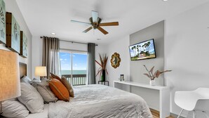 Ein modernes Schlafzimmer mit Bett, Deckenventilator, Fernseher und Blick ins Freie.