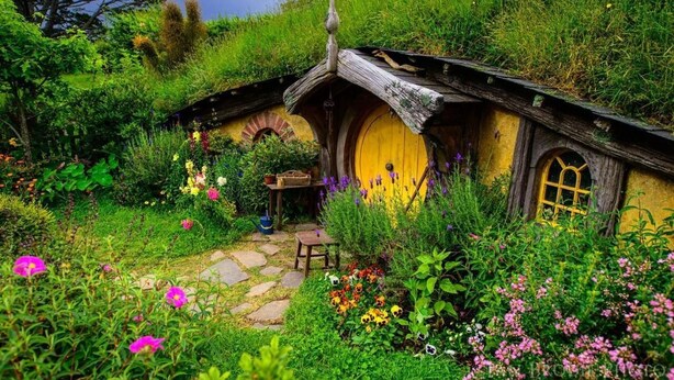 A Hobbit-style house with a yellow door, surrounded by lush greenery and colorful flowers. - Putaruru Arms Motor Inn (Putaruru)