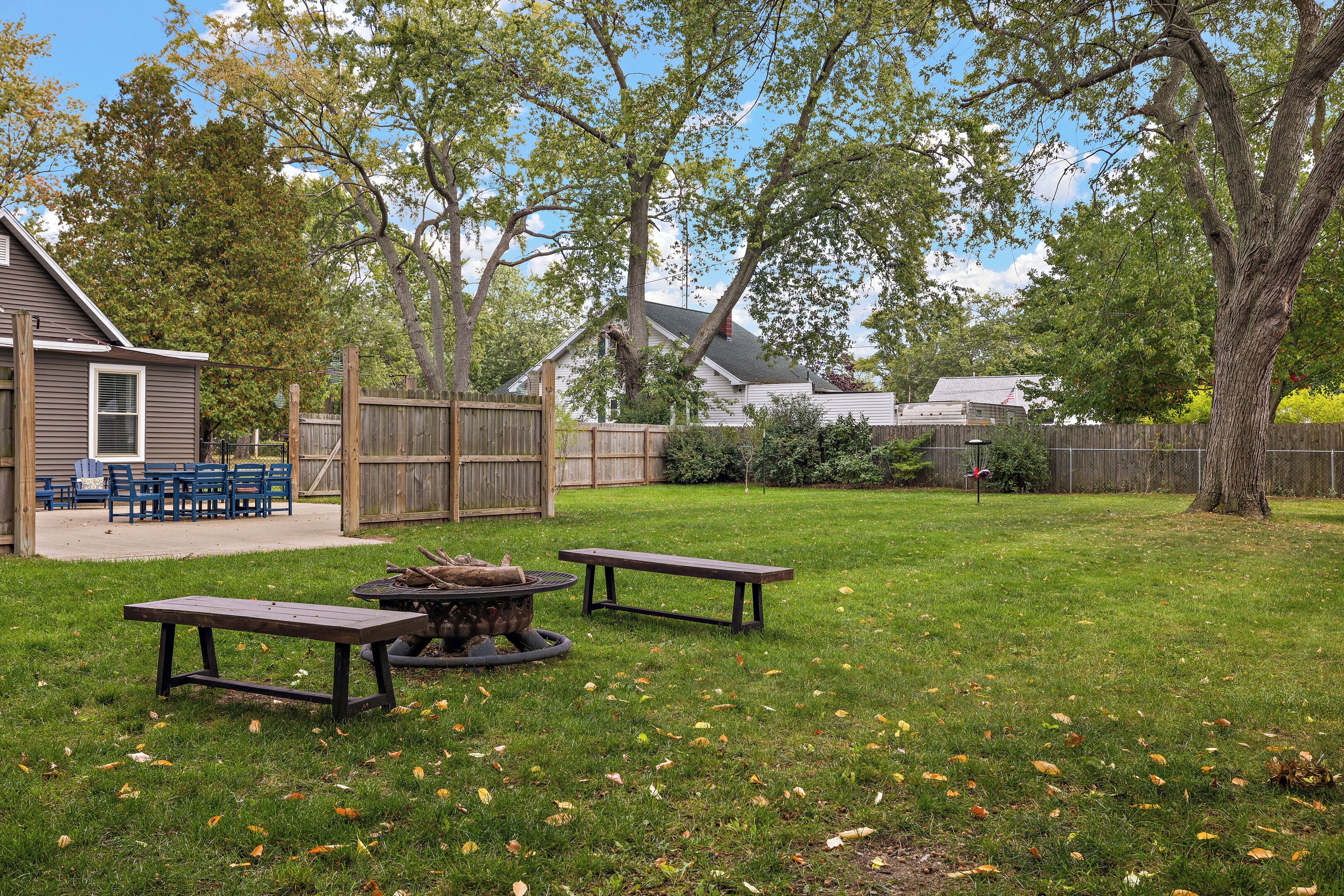 Ein Garten mit einer Holzterrasse, Picknicktischen und einer Feuerstelle.