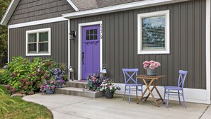 Una casa con una porta viola, una finestra e un portico con un tavolo e due sedie.