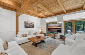 A modern living room with a white sofa set, a wooden coffee table, and a large TV screen.