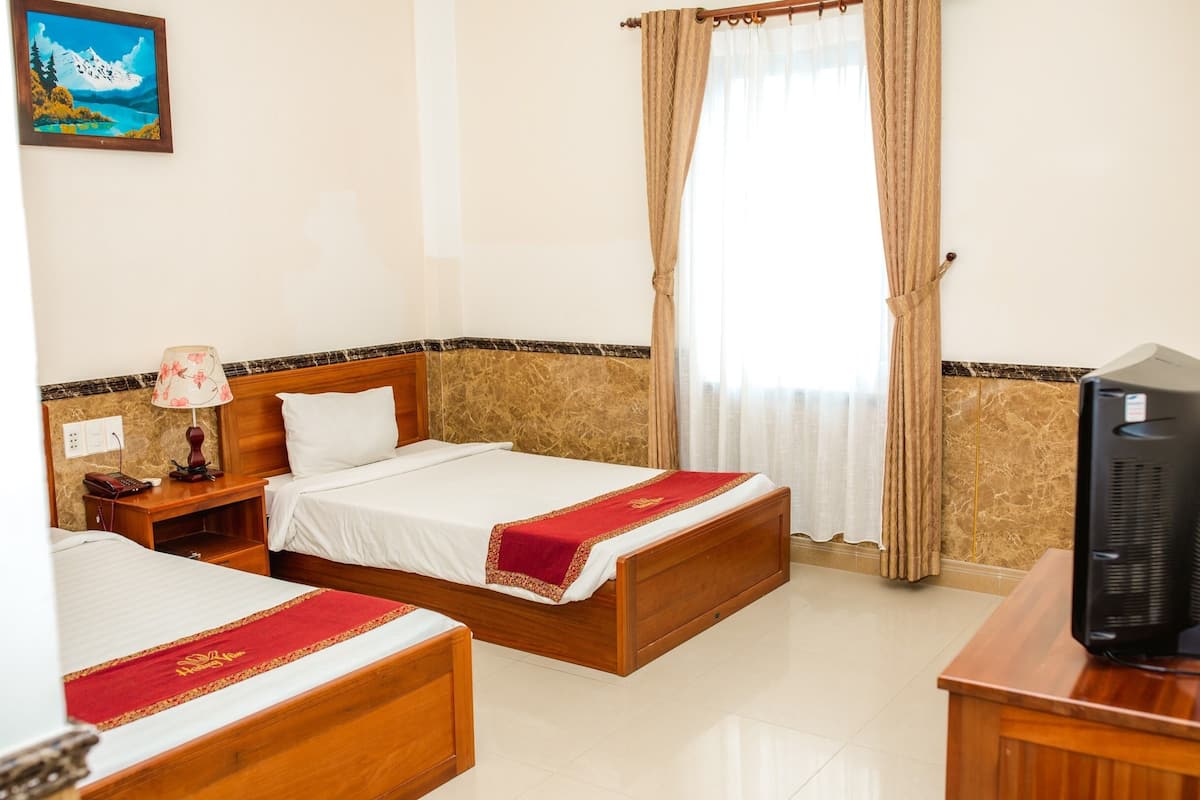 A hotel room with two beds, a television, a nightstand, a lamp, and a painting on the wall.