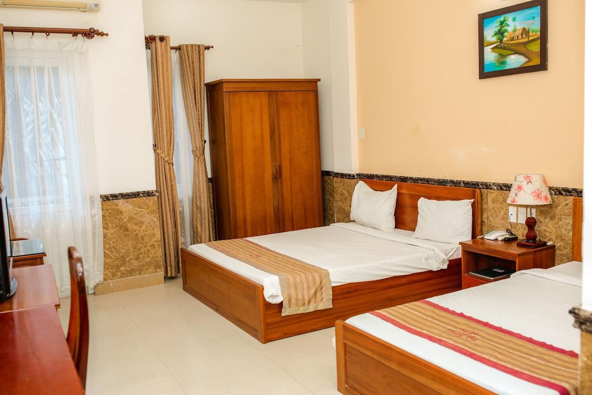 A hotel room with two wooden beds, a wooden wardrobe, a dining table, and a painting on the wall.