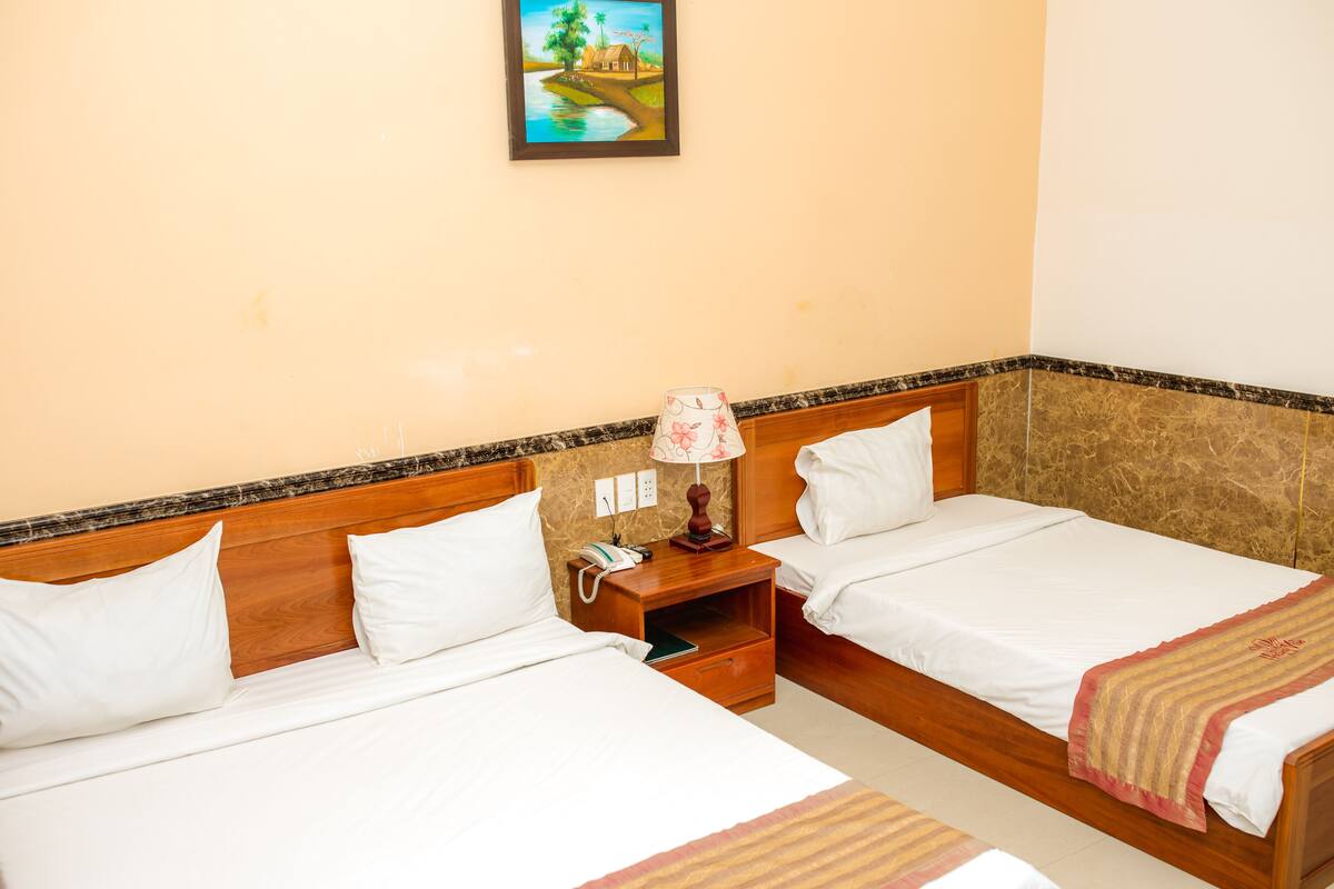 A hotel room with two beds, wooden headboards, a nightstand with a lamp, and a painting on the wall.