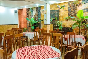 A restaurant with round tables covered with red and white checkered tablecloths, wooden chairs, and a variety of potted plants on the walls. - Hoang Van Hotel (Kon Tum)