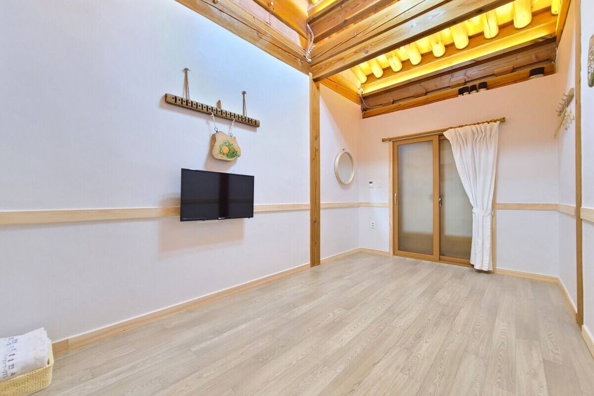 A room with a wooden floor, a flat-screen TV mounted on the wall, a small decorative item, and a sliding glass door with a white curtain.