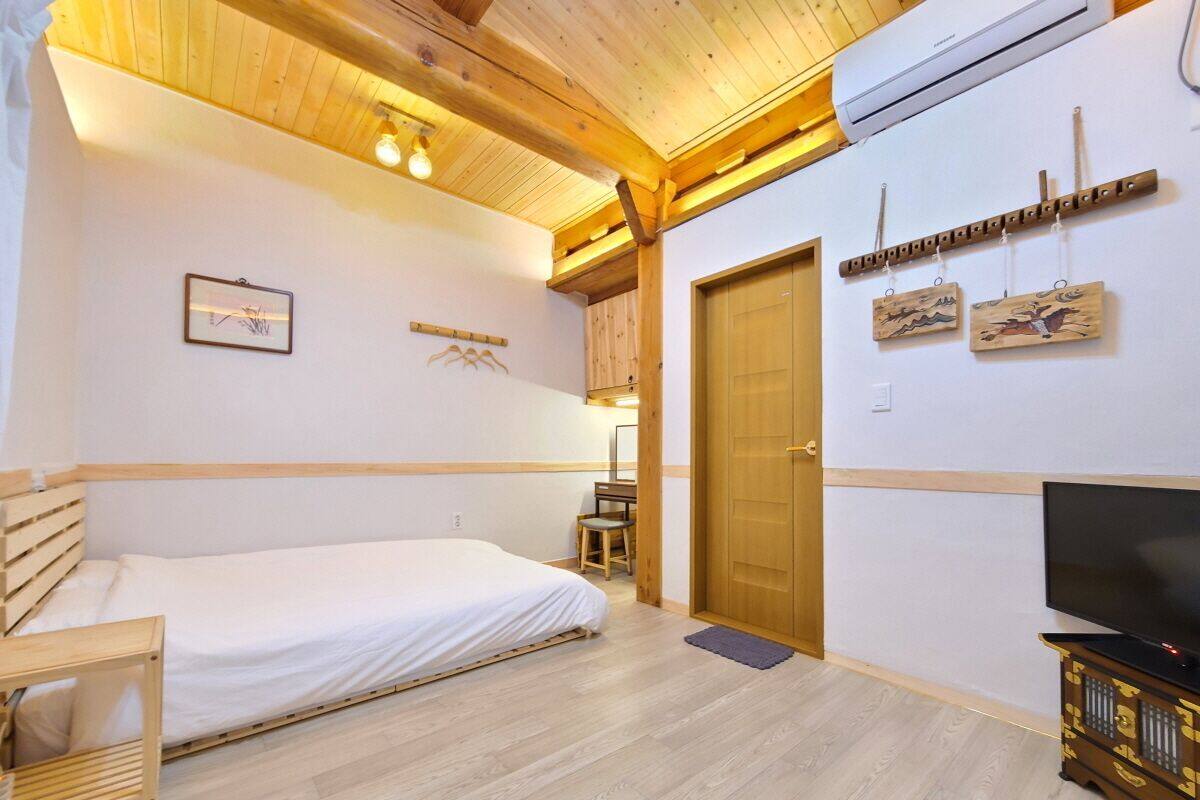 A bedroom with a bed, a chair, a desk, a television, and a door.