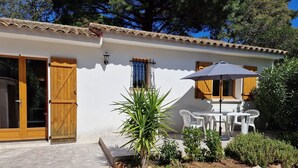 A white building with a tiled roof, wooden doors, and a patio area with a table and chairs. - PALOMBAGGIA VILLA AIR CONDITIONED 4 PERS less than 700 meters from the beach (Porto-Vecchio)