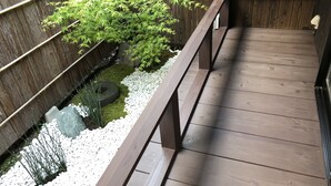 A wooden deck with a railing, surrounded by a bamboo plant and white pebbles.