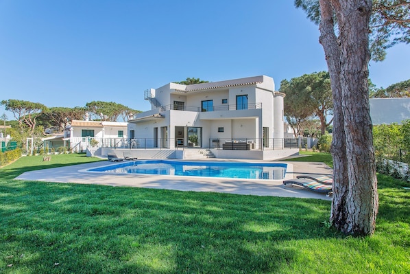 Una casa moderna de dos pisos con piscina, rodeada de césped cuidado y árboles.